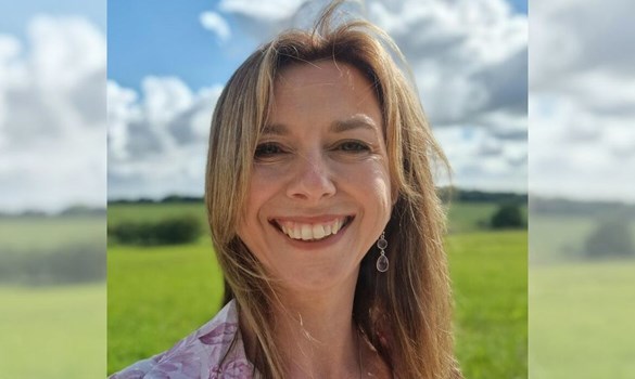 Headshot of a woman smiling to camera with a green grassy field in the background